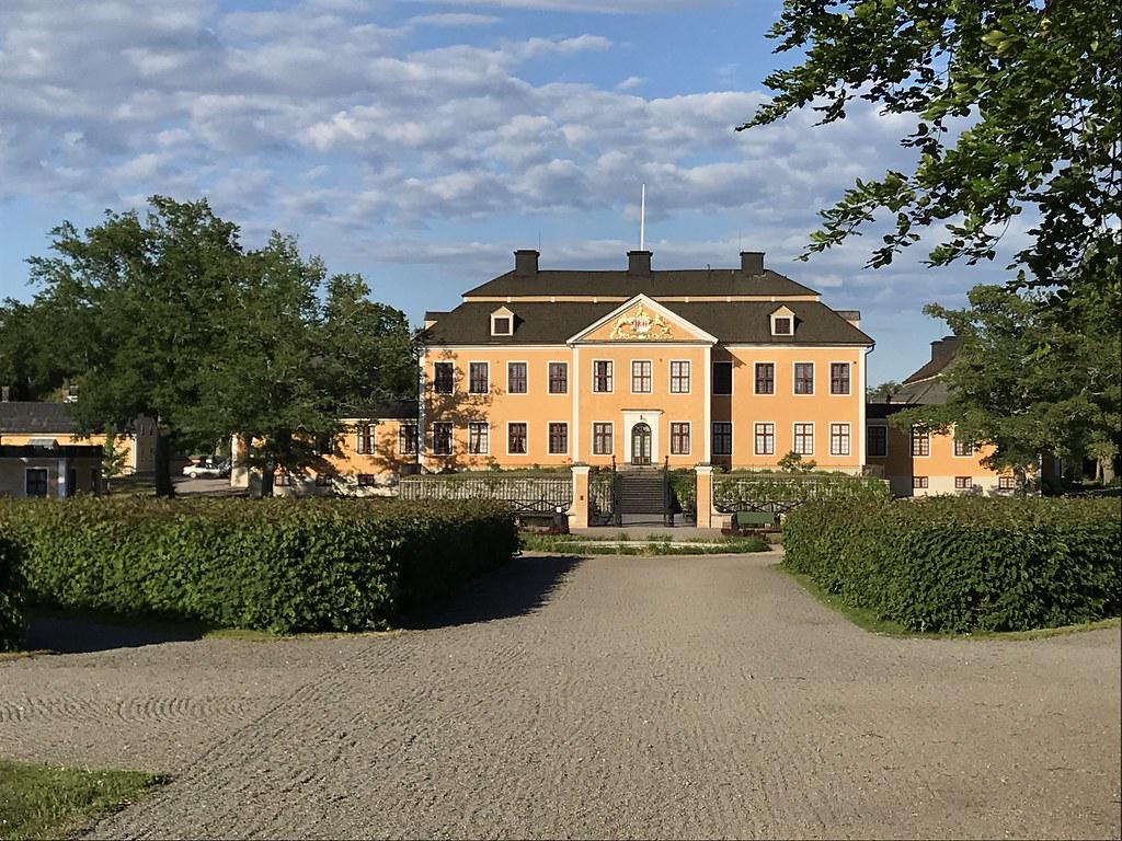 Saxå Bruks vackra trädgård med prunkande blommor och välskötta gräsmattor. I bakgrunden syns herrgårdens imponerande fasad och charmiga utomhusområden.